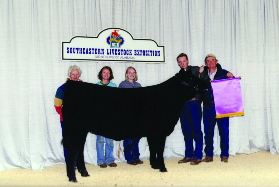 Participants pose with a prize-winning black cattle at the Southeastern Livestock Exposition in Montgomery, Alabama, showcasing their livestock and achievements in a competitive setting.